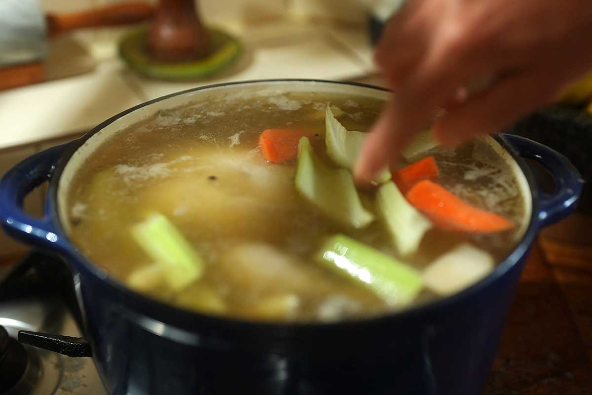 Carrots, turnips and celery being added to the pot around the chicken]