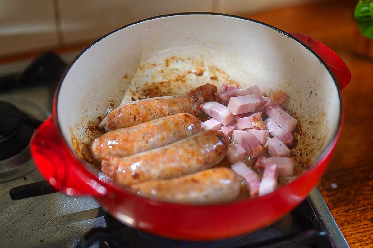 Sausages and bacon browning together in the same pot