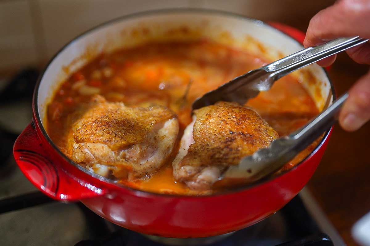 Sausages nestled into the beans, with chicken thighs placed on top skin-side up